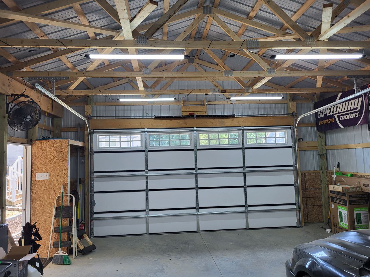Garage with white door, wooden roof trusses, tools, and storage.
